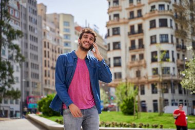 Mutlu, gülümseyen, beyaz, cep telefonu olan bir erkek büyük şehirde şehir caddesinde yürüyor, iş görüşmeleri yapıyor, cep telefonuyla konuşuyor..