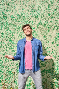 Sakallı adamın dikey portresi yeşil arka planda elleri açık kameraya bakıyor.