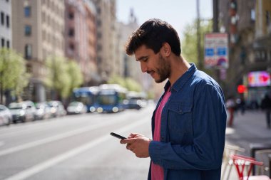 Güpegündüz trafik şeridinin yanında dururken akıllı telefon kullanan mutlu, esmer adam. Başvuru için taksi siparişi bekleniyor