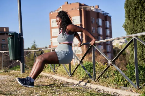 Sabah sporu. Korkuluklara dayanmış trisepsleri çalıştıran Afro-Amerikalı bir kadın..