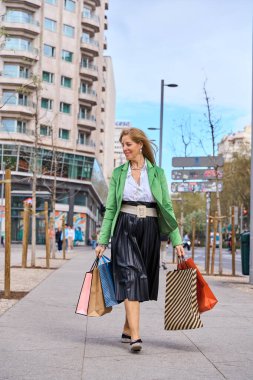 Zarif giysiler içinde elinde alışveriş torbalarıyla dolaşan bir kadın. Alışveriş ve yaşam tarzı kavramı