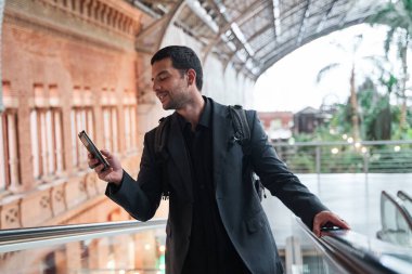 Sırt çantalı bir adam istasyondaki bir banliyö treniyle kapıya doğru gidiyor. Latin adam akıllı telefonunu kullanıyor.