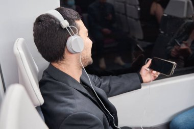Genç adam metroda oturup müzik dinlerken cep telefonu kullanıyor.