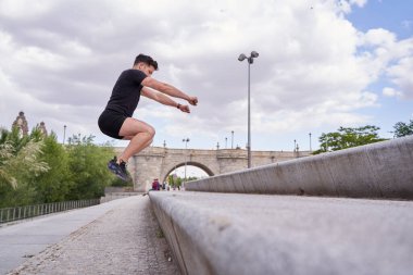 Atletik adam dışarıda antrenman yapıyor. Kutu atlayışı yapan genç Latin adam..