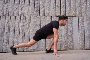 Sporcu adam koşmaya başladı. Genç adam çimento duvarının önünde koşuyor.