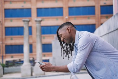 Afro-Amerikalı adam parkta akıllı telefon kullanarak kendine güveniyor.