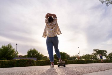 Gün batımında kaykayla ayakta duran tanınmayan bir kadının tam görüntüsü..