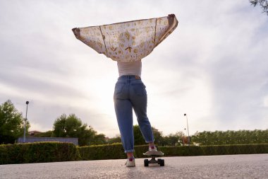 Gün batımında kaykayla ayakta duran tanınmayan bir kadının tam görüntüsü..