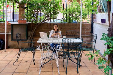 Öğrenci, bilgisayardan ders çalışmaya ara verdiğinde akıllı telefonunu kullanarak evinin avlusunda..