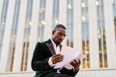 Takım elbiseli genç işadamı iş toplantısına geçmeden önce belgelere bakıyor.