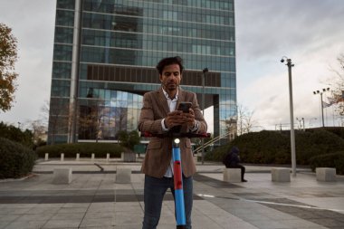 İş adamı akıllı telefonunu scooterında kullanıyor. yeşil ulaşım aracı