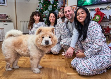 Bir köpek de dahil olmak üzere beş kişilik bir aile pijamalı bir resim için poz veriyor. Köpek ailenin önünde duruyor, ve aile üyeleri de yerde oturuyorlardı. Sahne sıcak ve rahat.