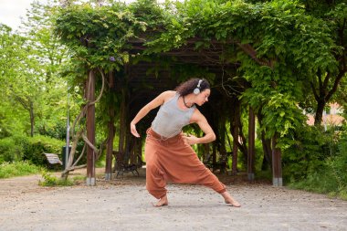 A contemporary dancer moves gracefully in a park, immersed in music through headphones, blending artistry with nature's serenity. clipart