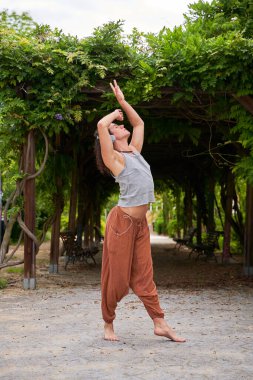 A contemporary dancer moves gracefully in a park, immersed in music through headphones, blending artistry with nature's serenity. clipart