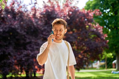 Sakallı genç bir Latin adam akıllı telefonuyla konuşurken gülümsüyor, günlük yaşamında bir neşe ve bağlantı anı yakalıyor..