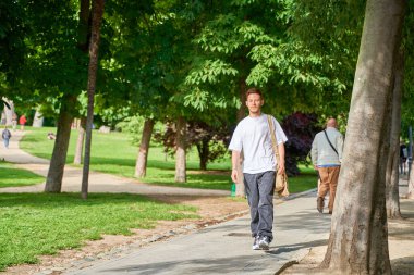 Genç bir Latin, parkın içinde huzur içinde yürüyüp doğal çevreyi ve temiz havayı seyrediyor..