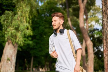 Bir adam parkta yürüyor, kolunun altında bir kitap taşıyor, doğa ile çevrili huzurlu bir yürüyüşün tadını çıkarıyor ve bir an için okumaya hazır..