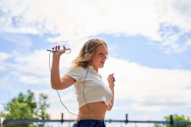 Kendine güvenen genç bir kadın müzik dinliyor ve sokakta dans ediyor.