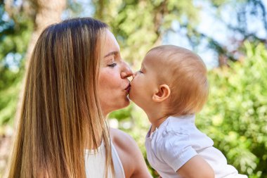 Bir kadın bir bebeği öper. Bebek beyaz bir gömlek giyiyor.
