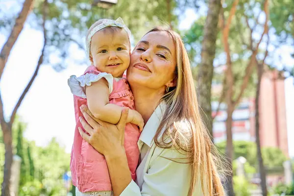Anne parkta bebeğini kucağında tutuyor ve gülümsüyor.