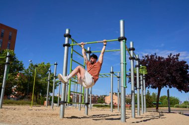 Kafkasyalı bir adam barın üzerinde sallanan bacağını kaldırır, karın egzersizinde vücut gücünü ve zindeliğini gösterir..