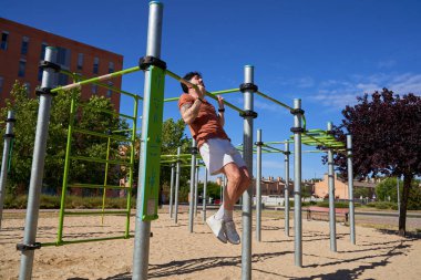 Genç bir atlet, açık hava idman ortamında güç ve adanmışlığını göstermek için açık hava spor parkında barfiks çekiyor..