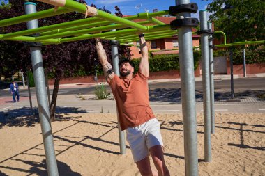 Genç bir atlet, açık hava idman ortamında güç ve adanmışlığını göstermek için açık hava spor parkında barfiks çekiyor..