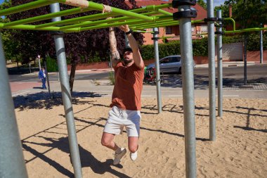 Genç bir atlet, açık hava idman ortamında güç ve adanmışlığını göstermek için açık hava spor parkında barfiks çekiyor..