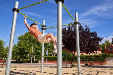 Genç bir atlet, açık hava idman ortamında güç ve adanmışlığını göstermek için açık hava spor parkında barfiks çekiyor..