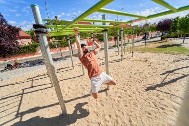 Bir adam açık hava ortamında fiziksel kondisyon, azim ve dayanıklılık göstererek, açık hava jimnastik parkında yoğun bir antrenman yapar..