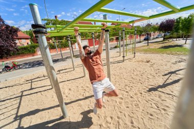Bir adam açık hava ortamında fiziksel kondisyon, azim ve dayanıklılık göstererek, açık hava jimnastik parkında yoğun bir antrenman yapar..