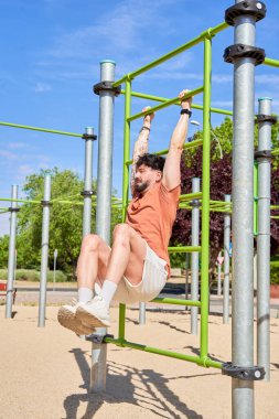 Kafkasyalı bir adam barın üzerinde sallanan bacağını kaldırır, karın egzersizinde vücut gücünü ve zindeliğini gösterir..
