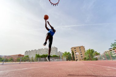 Siyah basketbolcu açık alanda smaç basıyor.