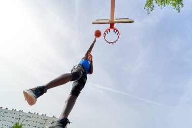 Siyah basketbolcu açık alanda smaç basıyor.