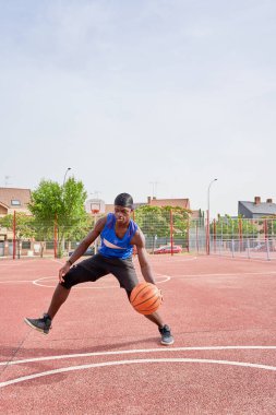 Mavi gömlekli bir adam kortta basketbol oynuyor. Elinde bir basketbol topu tutuyor.