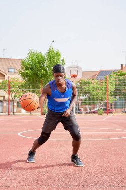 Mavi gömlekli bir adam kortta basketbol oynuyor. Elinde bir basketbol topu tutuyor.