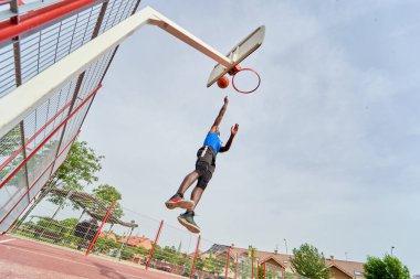 Siyah basketbolcu açık alanda smaç basıyor.