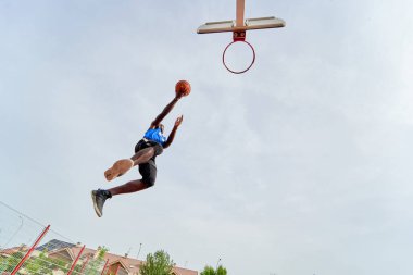 Siyah basketbolcu açık alanda smaç basıyor.