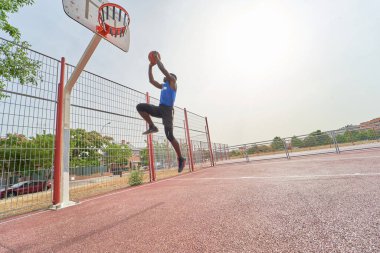 Siyah basketbolcu açık alanda smaç basıyor.