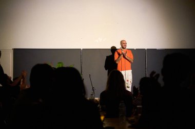 Kafası tıraşlı bir erkek oyuncu seyircilerle dolu alternatif bir tiyatroda sahnede monolog yapıyor.