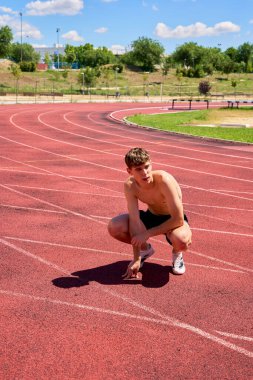 Tişörtsüz sporcu antrenman sırasında yolda çömeliyor.