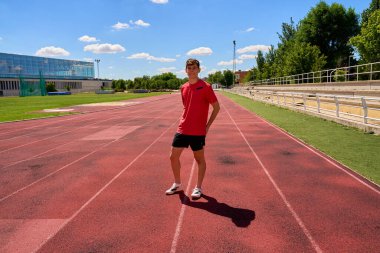 Kırmızı tişörtlü ve şortlu bir adam raylarda dikiliyor.
