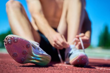 Ayakları havada bir adam yerde oturuyor. Altında çivi olan beyaz ayakkabılar giyiyor.