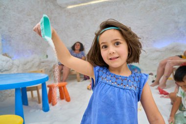 Girl playing with salt in a salt cave during halotherapy session clipart