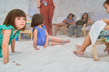 Çocuklar içeride beyaz kumda oynuyor ve dinleniyorlar.