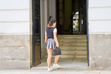 Genç bir kadın bir çantayla binaya giriyor.