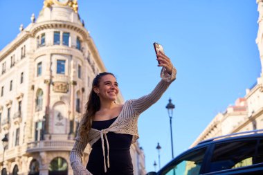 Young Caucasian woman taking selfie in front of historic architecture clipart