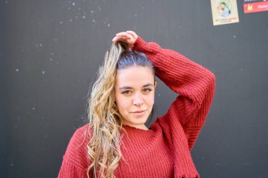 Kızıl kazak giyen beyaz bir kadın saçını düzeltiyor.