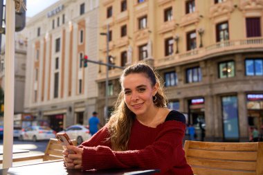 Açık kafede akıllı telefonlu gülümseyen beyaz bir kadın.