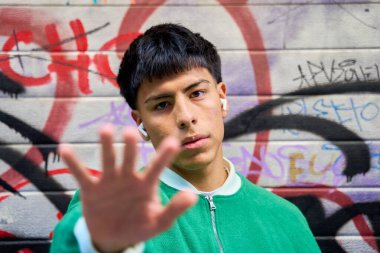 Duvarın önünde el kaldırmış genç Latin bir adam.